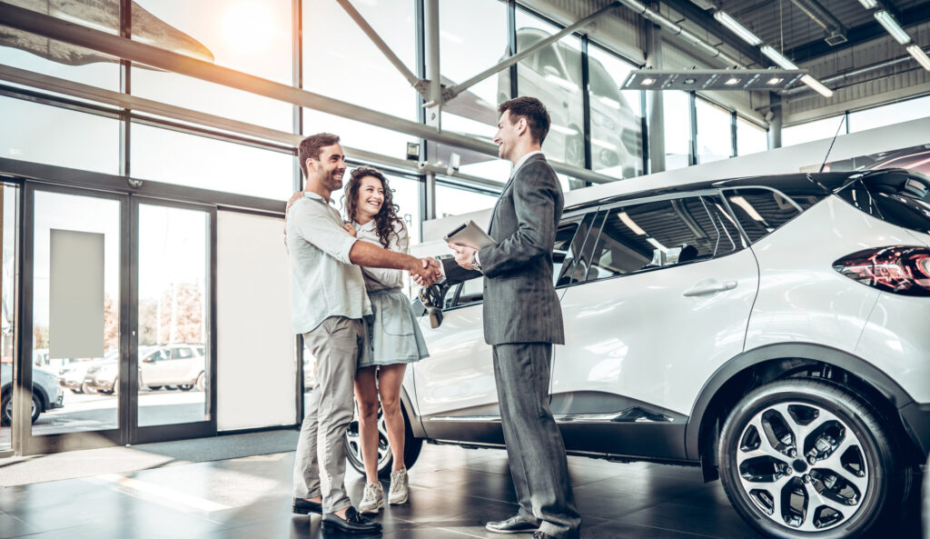 Couple completing purchase of a car inside dealership with car salesman