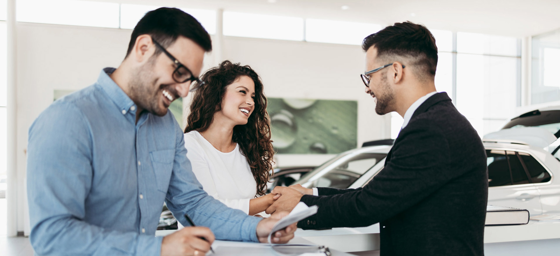 Happy customers signing car contract inside shop with car dealer