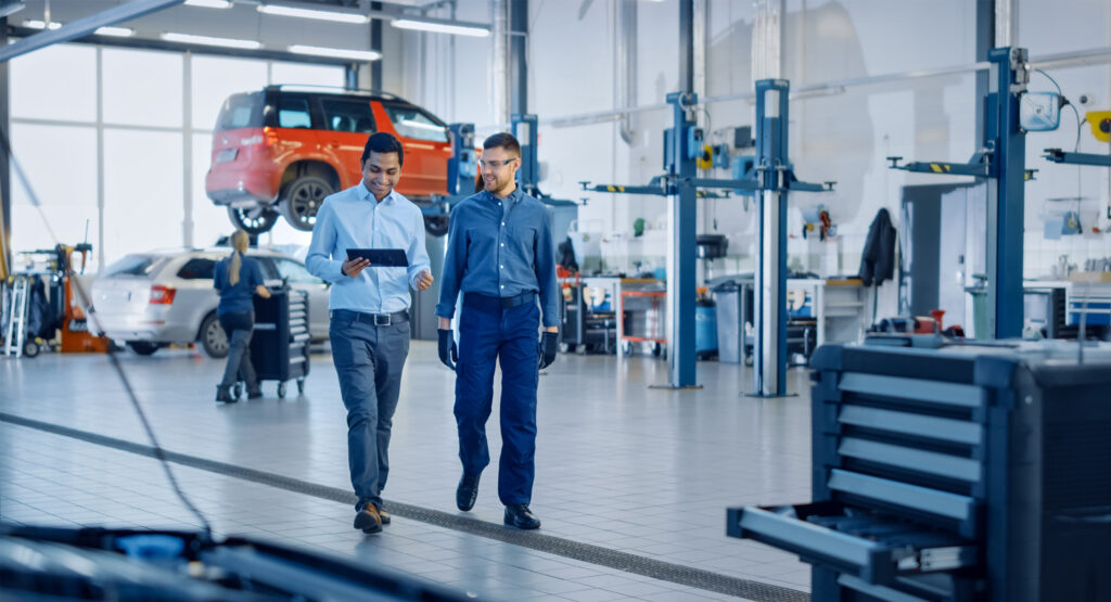 2 Mechanics looking at Identifix data on tablet walking through a vehicle repair shop